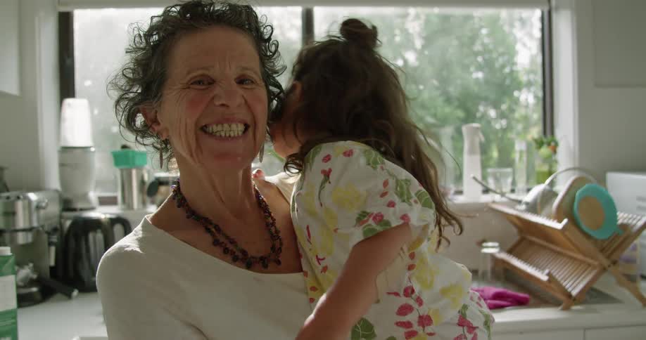 Happy grandmother holding her granddaughter on her hands in the kitchen at home