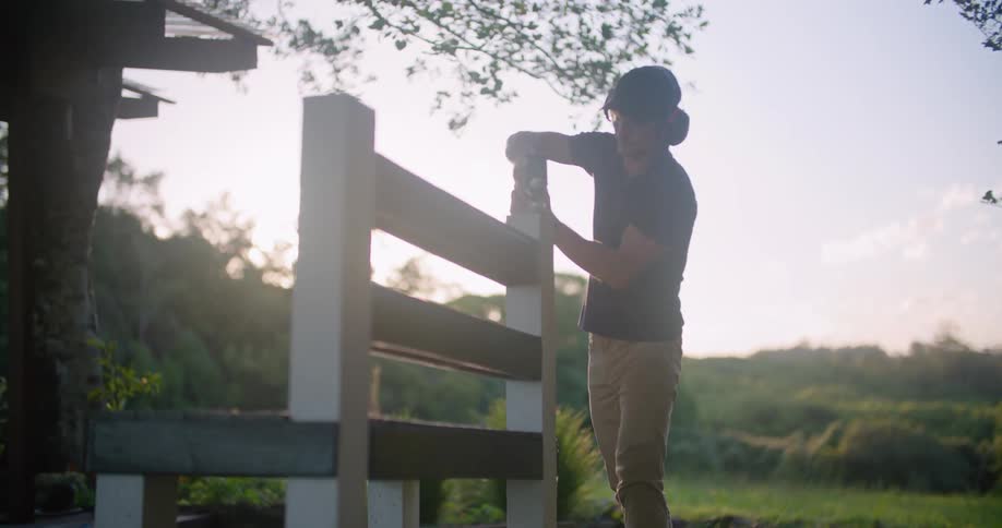 Man stands outdoors working on bench with field in background