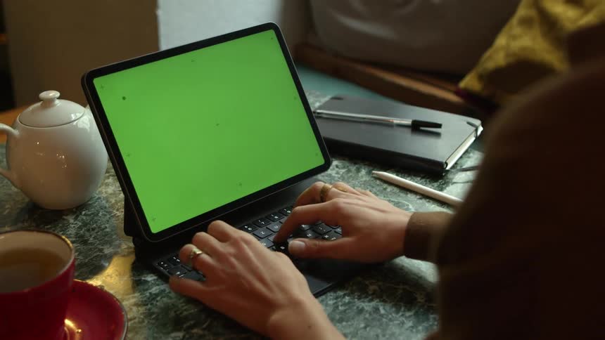 Woman typing on the keyboard of a laptop with a green replaceable screen
