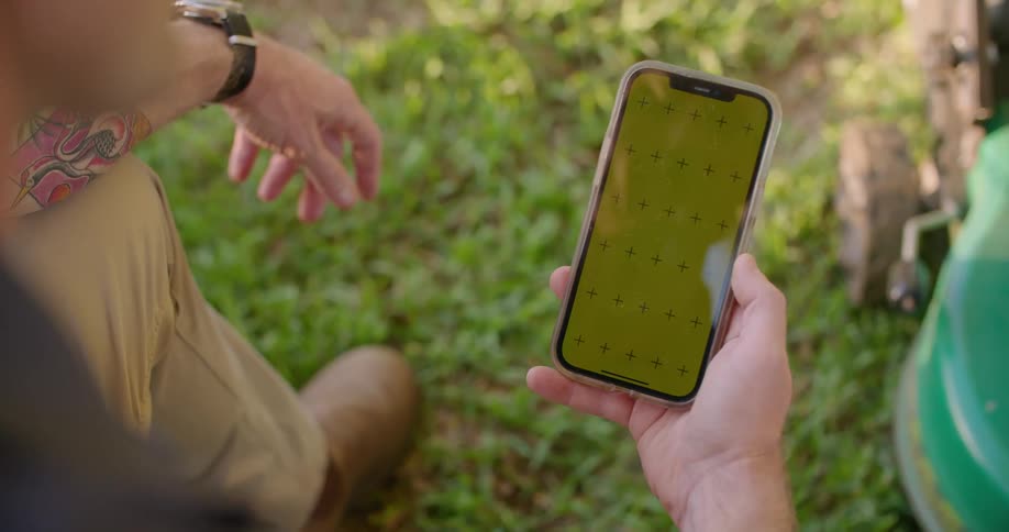 Man standing near a lawnmower uses a smartphone with a green replaceable screen