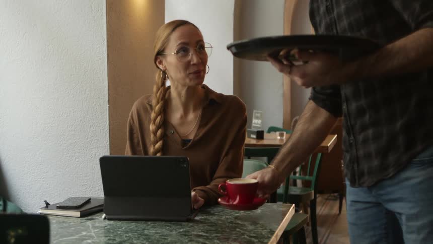 A waiter serves coffee to a customer using a tablet