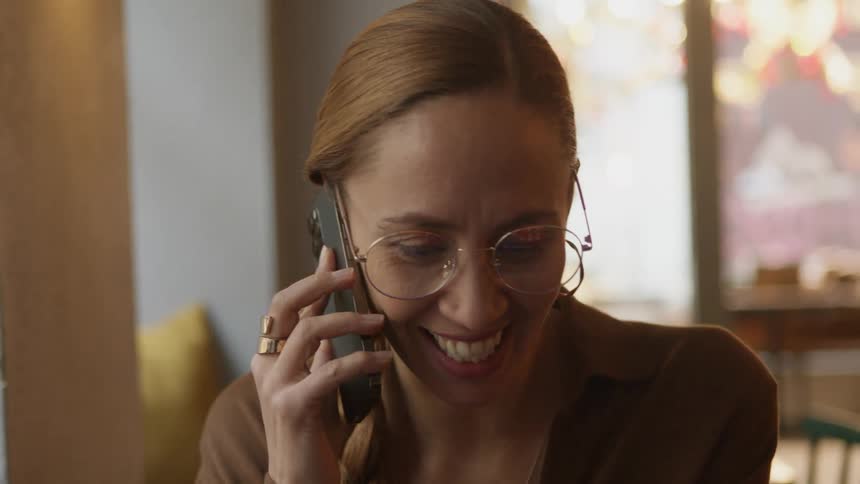 A woman smiles while talking on her smartphone indoors during the day