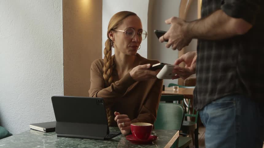 Woman sitting at a table in a restaurant uses her smartphone to pay the bill
