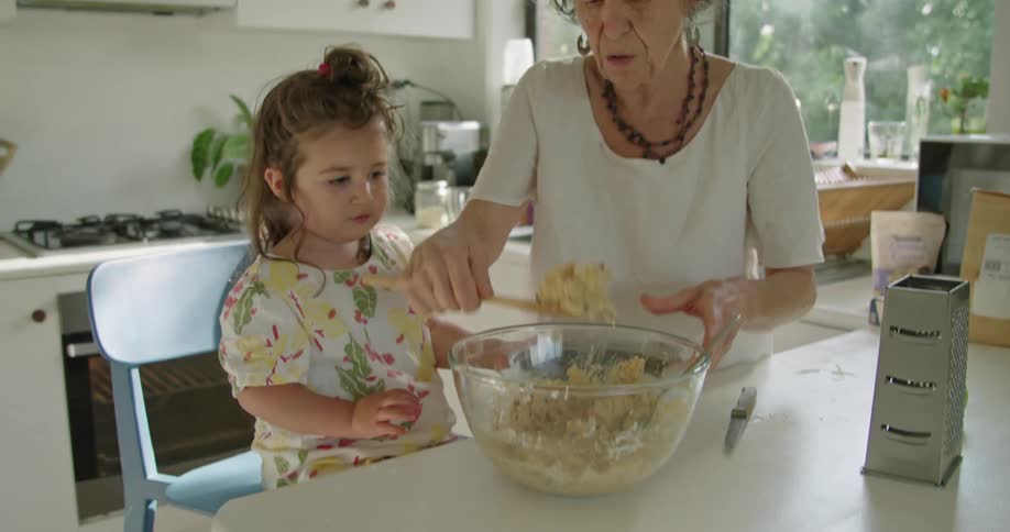 A grandmother is showing her granddaughter how to cook