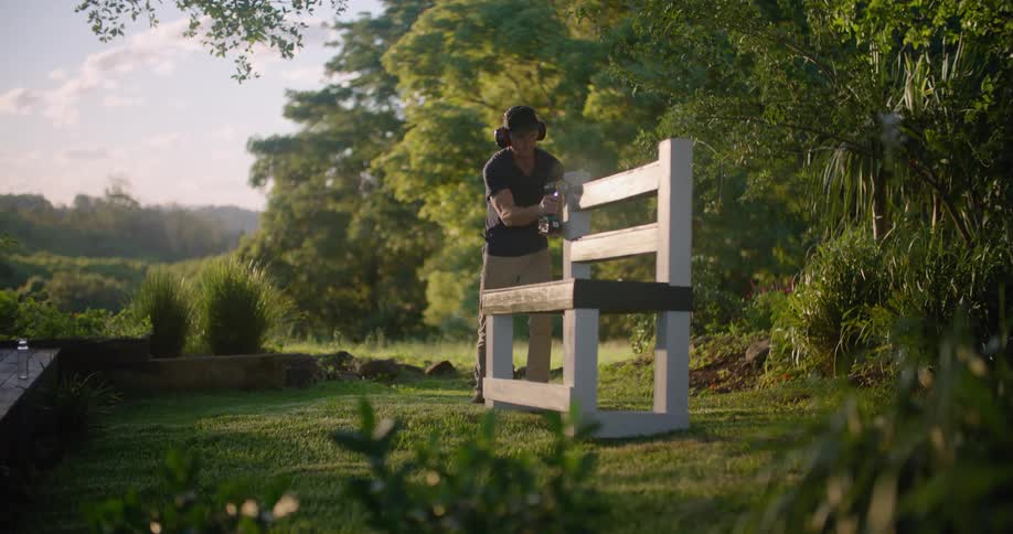 A man stands in a grassy field and builds a bench