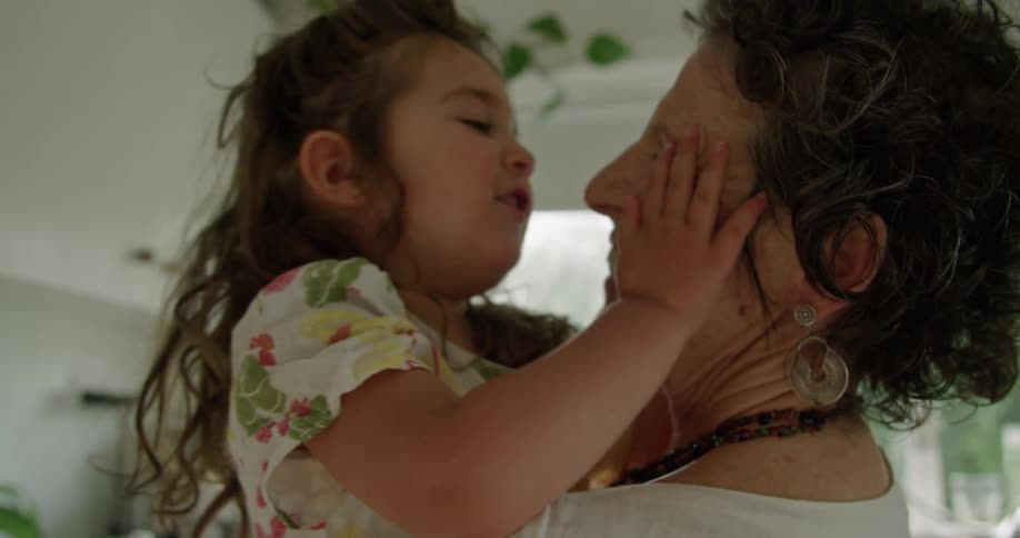 A grandmother holds her granddaughter in her arms and they hug and rub noses together