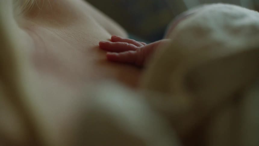 Newborn baby wrapped on a blanket resting over mother's chest breastfeeding