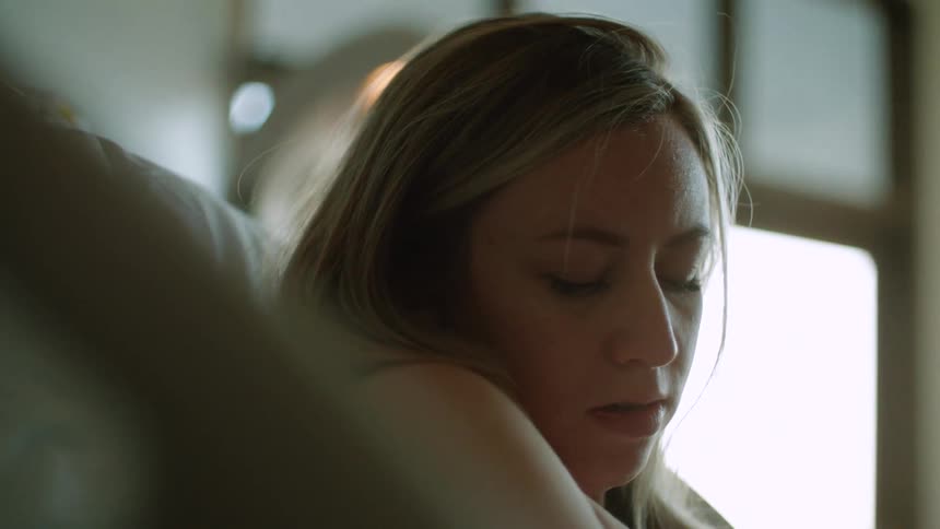 A mom sitting up against a pillow looking down caressing an infant