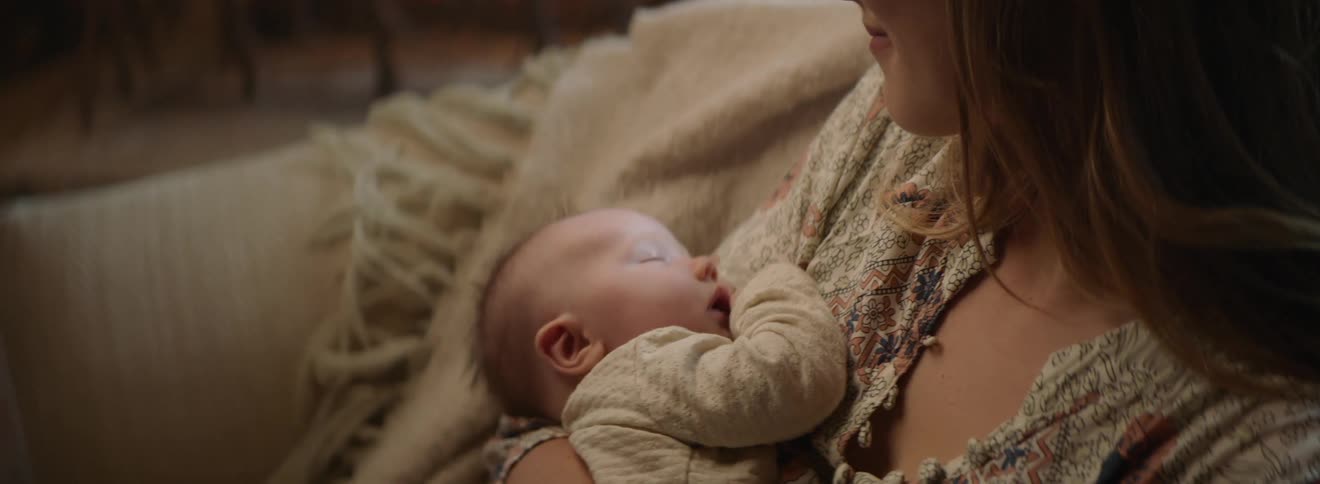 A woman smiles as she looks down at the sleeping baby shes holding