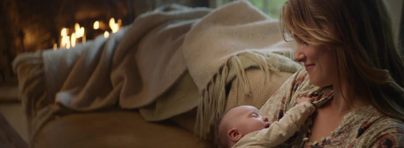 A mother is smiling while holding her infant daughter and watching her smile in her sleep