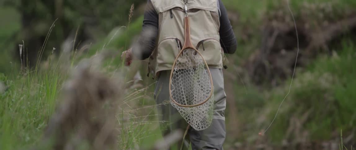 A man carrying a net and pole walks through tall grass