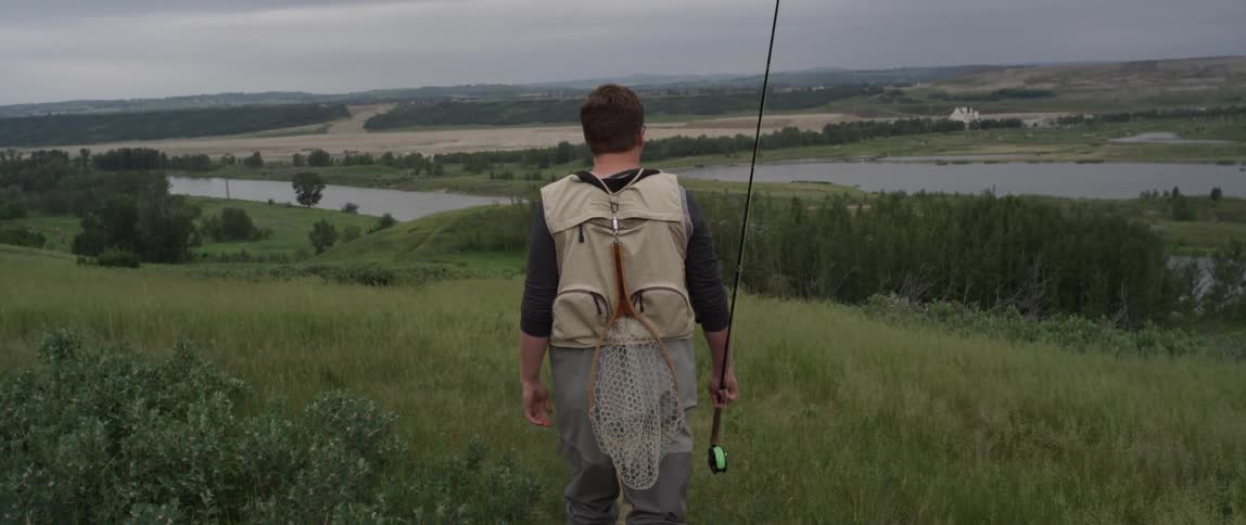 A man carrying a fishing pole walks towards a river