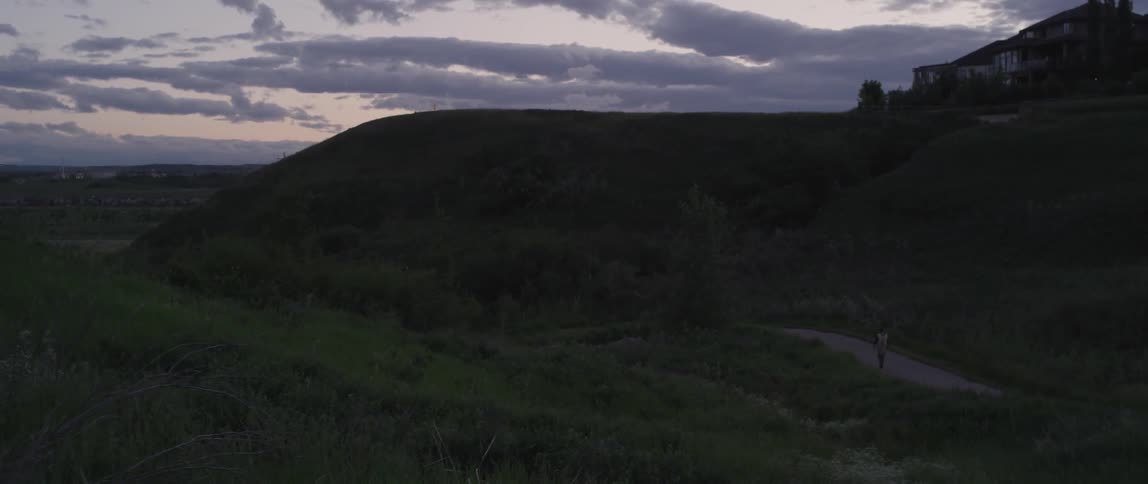 A person is walking along a tail near a steep hill at sunset