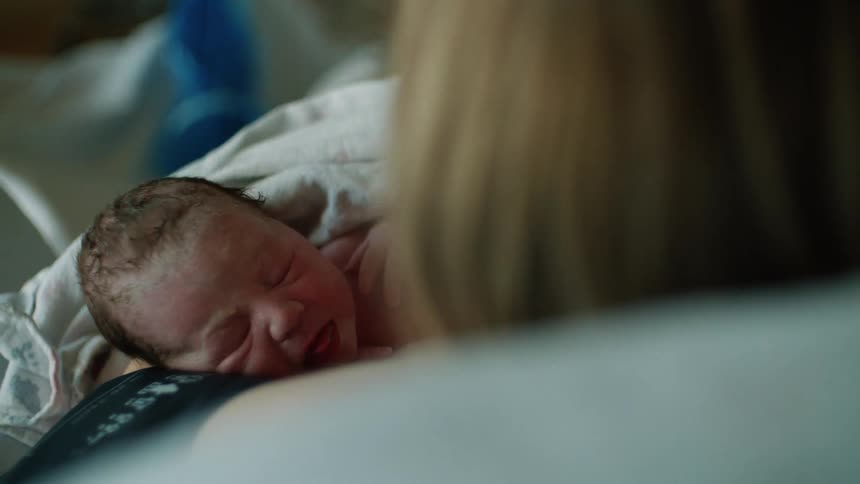 Mom pulls blanket up to cover her newborn baby as they lie together in a hospital bed