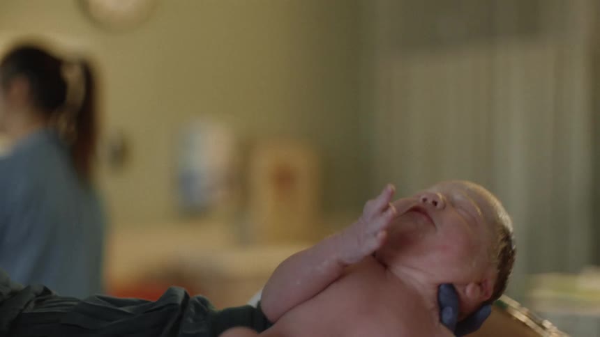 Nurse places a newborn baby in a mothers arms in a hospital delivery room