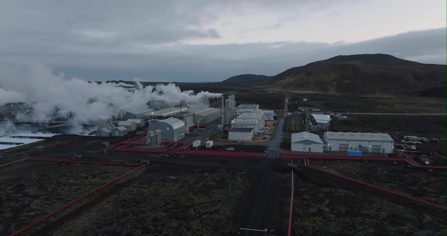 Heavy smoke billows from a large factory in the countryside
