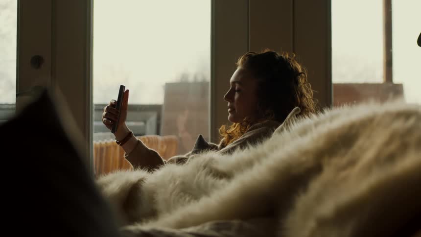 A woman is sitting on the couch and talking to someone on her phone