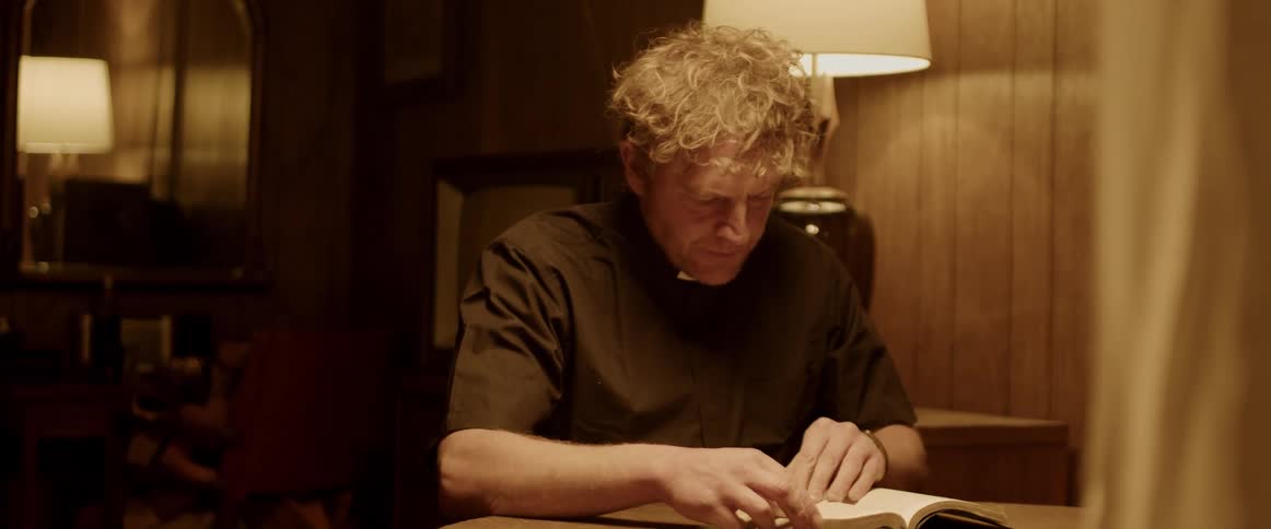 A man is sitting at a table and reading a book at night