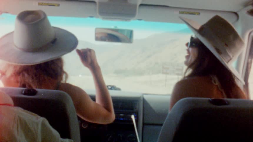 Two women wearing white sunhats are riding in a car and getting into the music as they drive