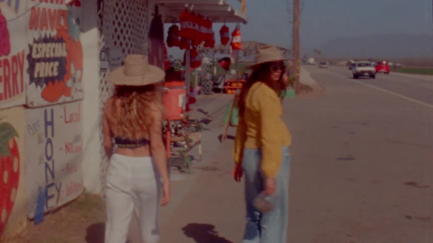 Two women wearing hats are walking and smiling near a farmers market store