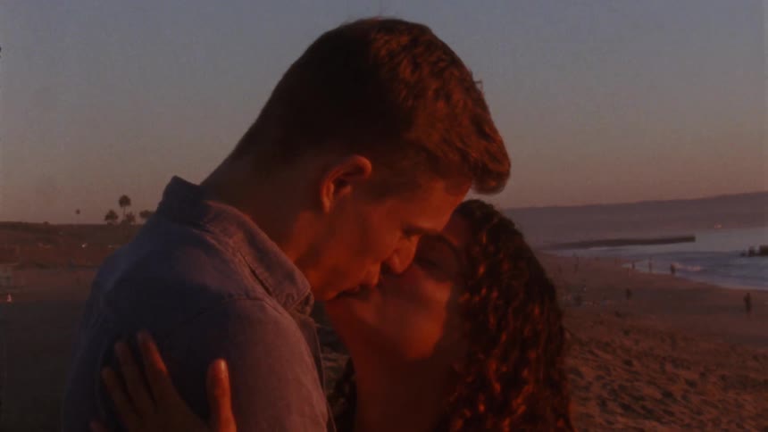 A man and woman stand on a beach and kiss