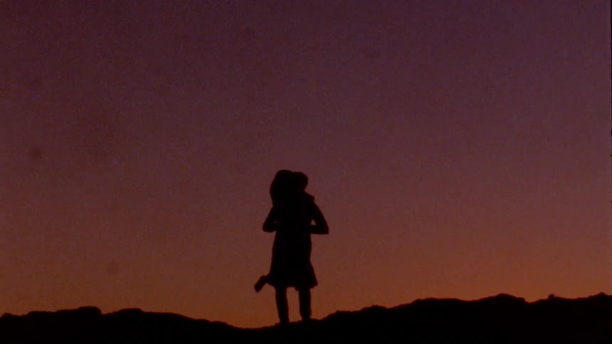 A silhouette of a couple standing on rocks kissing and hugging at sunset