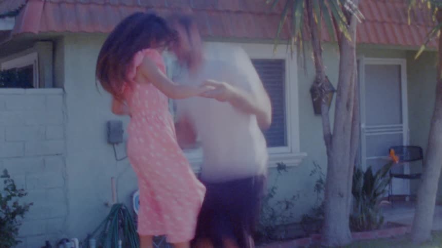 Timelapse of a man holding hands with his daughter as they jump on a trampoline outside a house