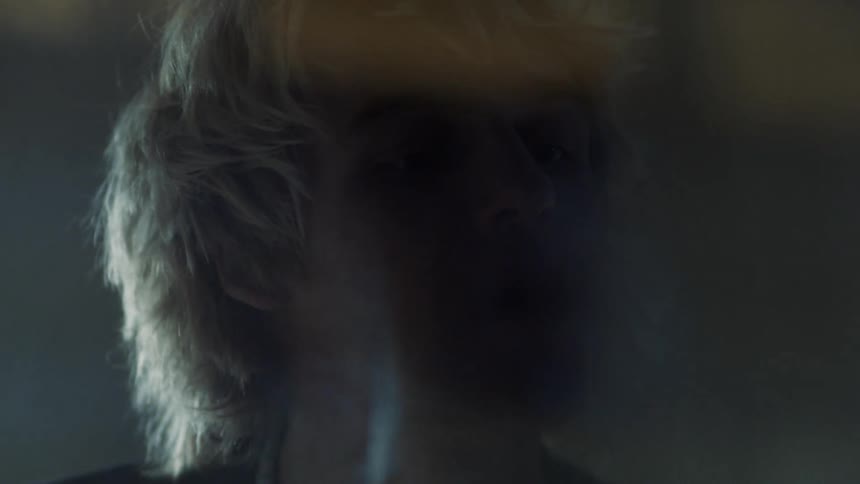 A man looks into a window and blows on it then draws a heart on the glass