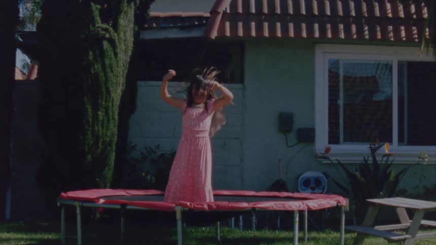 A young girl jumps on a trampoline outside her home