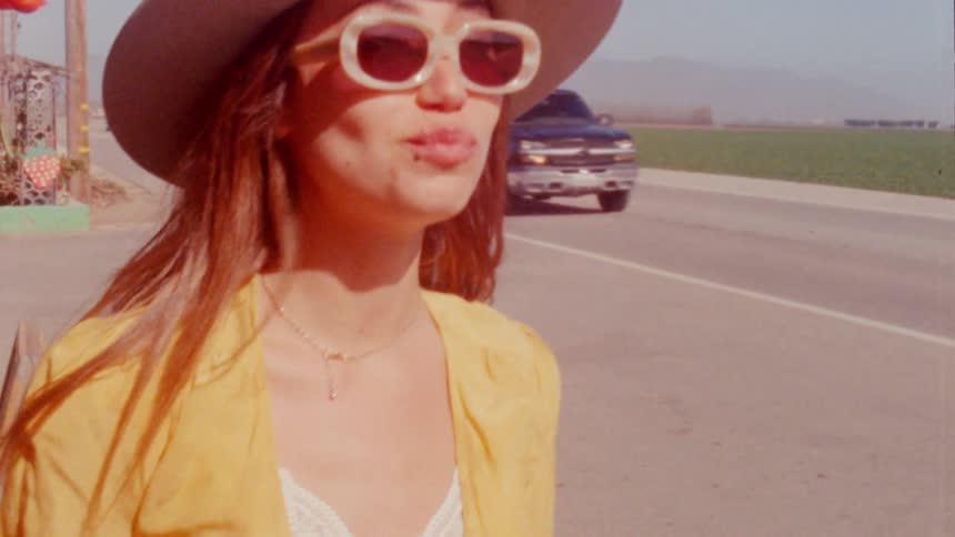 A woman is standing on the side of a road where cars are driving by