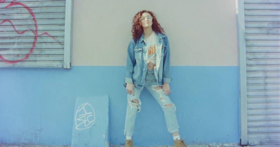 A woman leans against a wall and poses for a portrait