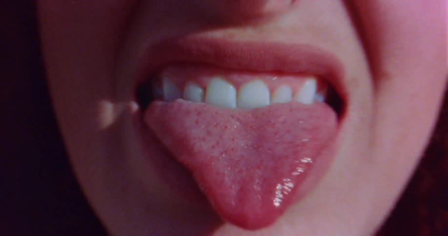 A womans pink tongue sticking out of her mouth as she grimaces