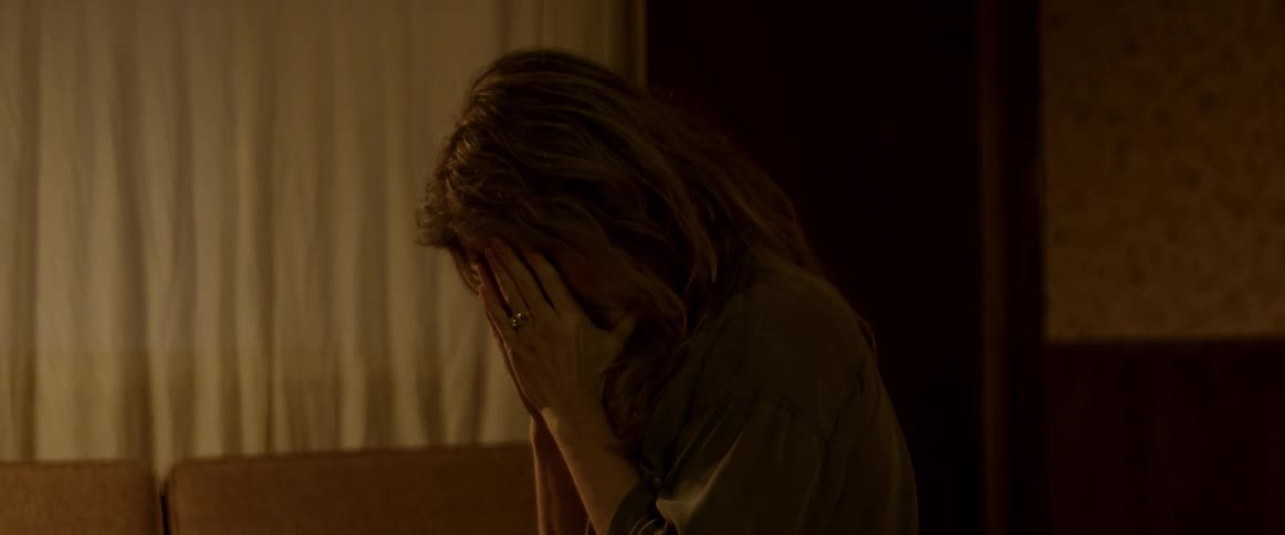 A woman is sitting down in a dark room and puts her head in her hands