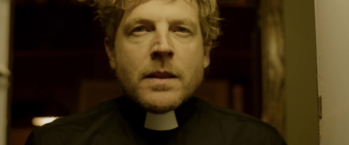 A priest is looking ahead and appears to be troubled