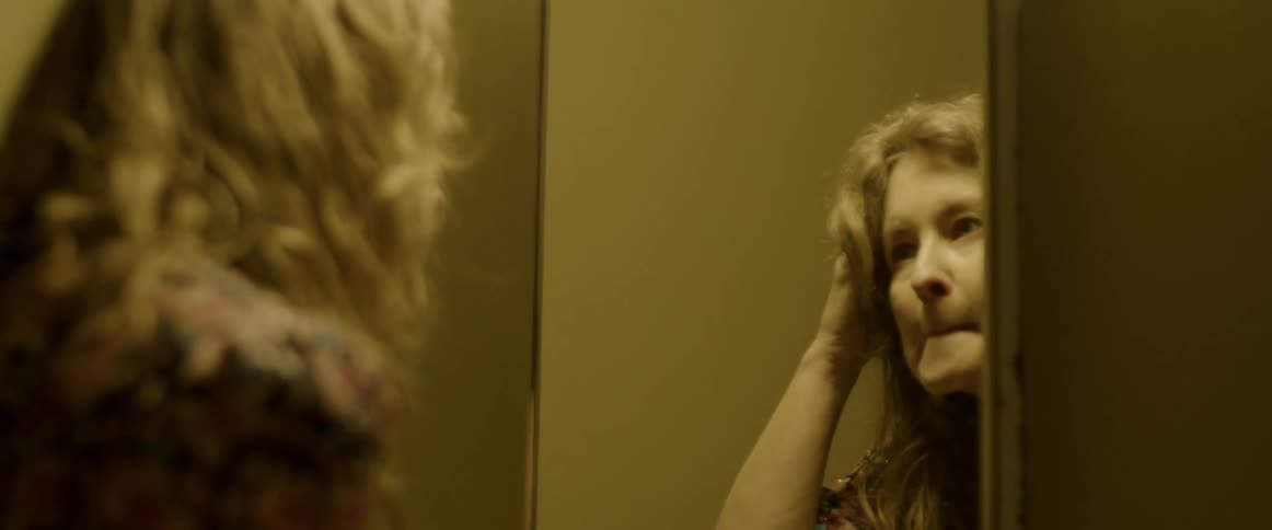 Woman touching her lips and hair looking at herself in a mirror inside a room