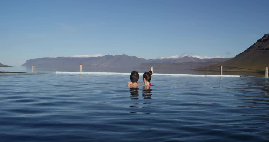 A man and woman are embracing in a pool facing a mountain range