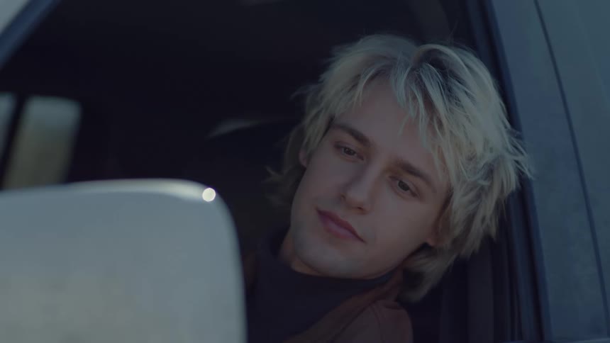 A man smiles as he looks at his own reflection in a car side mirror