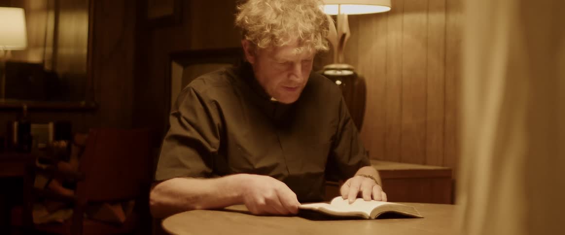 Reverend sits at small wooden table with a bible