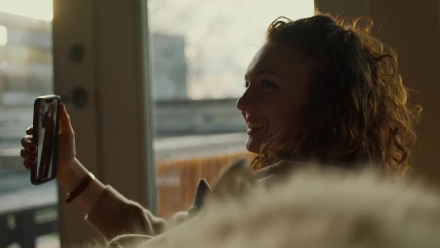 Woman sitting on a couch at home in the morning looking at a video on her smartphone