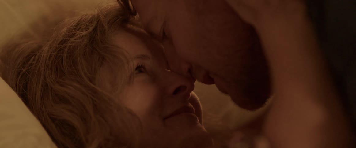 Man and woman hold each other and lovingly look into each others eyes while lying down on bed in bedroom