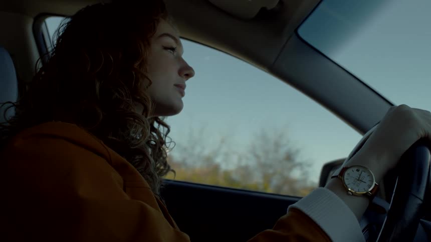 A woman drives along a highway lined with trees