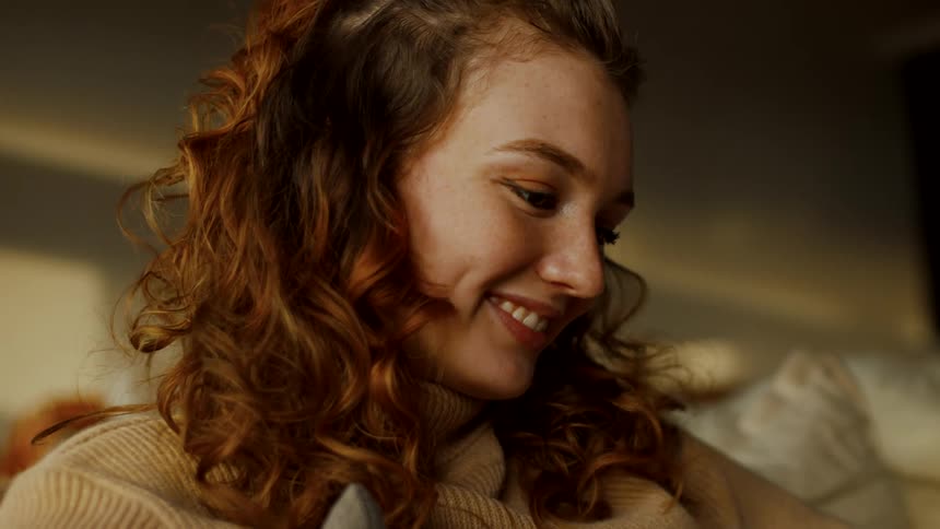 A woman is standing inside a house looking at something and then she looks up at someone and smiles