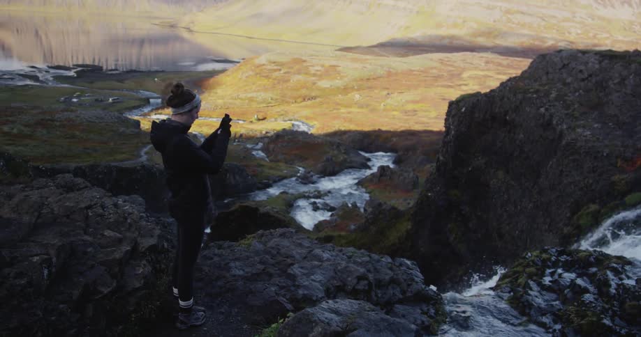A woman takes a photograph on the edge of a waterfall