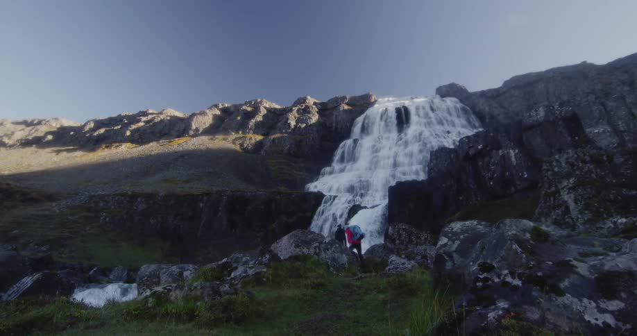 A waterfall is pouring downhill as two people climb up to the foot