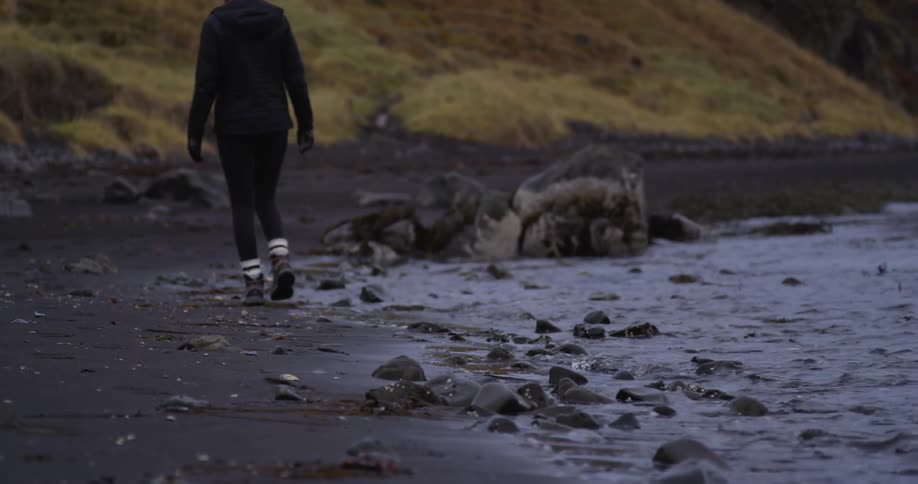 A woman is walking along the water of a shore
