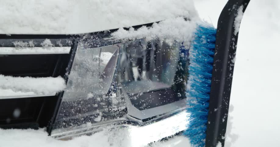 A person brushes off their headlight as it snows
