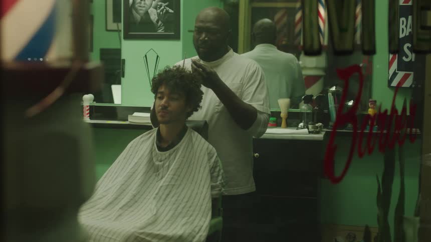 Bald barber with white t shirt and beard cuts mans curly hair with scissors holding hair and being possessed by fear all of a sudden in barber shop