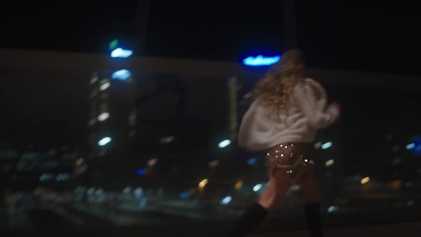 A woman runs twirls and leaps joyfully on a pedestrian bridge over a highway