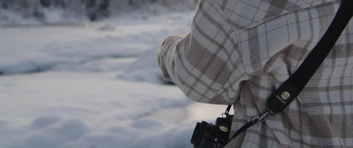 A person outside in the wilderness snow with a camera fixes their gloves