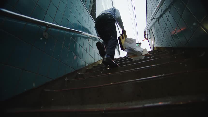 Man with shirt tie pants and black shoes goes up stairs and documents fall out of briefcase